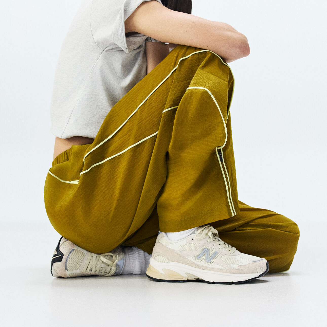 Knee-down of a woman sitting wearing New Balance sneakers on a white background